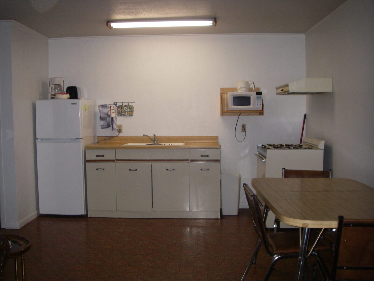A kitchen with a table and chairs, refrigerator, microwave, sink and oven.